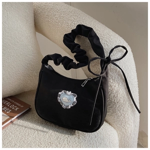 Detail of black canvas bag featuring heart patch and ruched strap on a white sofa