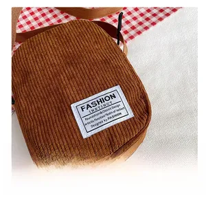 Detailed view of a brown corduroy crossbody bag with a fashion logo patch and fabric strap