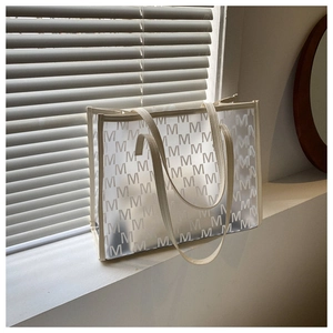 Detail of trendy semi-transparent tote bag with M-letter print and beige leather straps