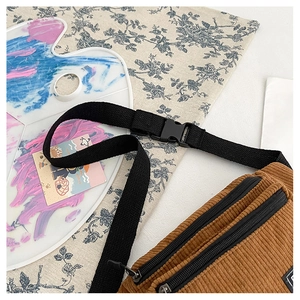 Detail of brown corduroy waist bag showing dual zippers and black nylon buckle strap