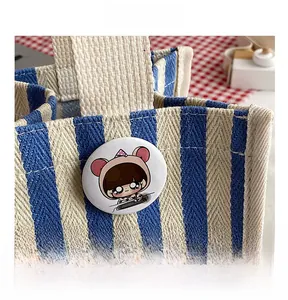Close-up of blue and white striped canvas handbag featuring a cute cartoon badge accessory