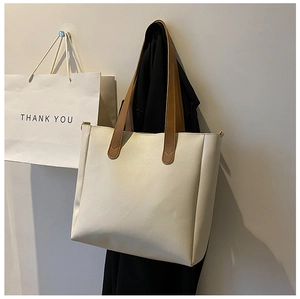 Close-up of cream faux leather tote bag with brown straps hanging in a minimalist setting