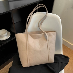 Minimalist beige tote bag with geometric triangle quilting on a stylish modern chair