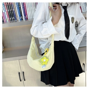 Détail d'un sac demi-lune en toile jaune avec charm floral porté sur un style écolière