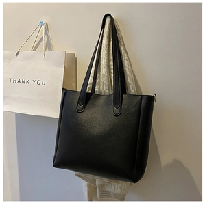 Detail of a large black soft leather tote bag hanging in a minimalist setting