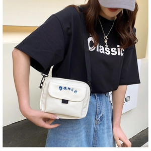 Detail of white nylon crossbody bag featuring blue Dance embroidery and black strap