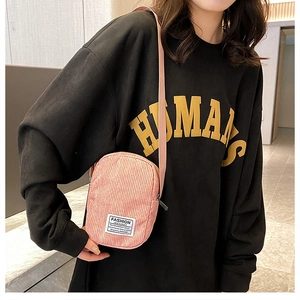 Detailed view of mini pink corduroy crossbody bag with woven label on model's shoulder