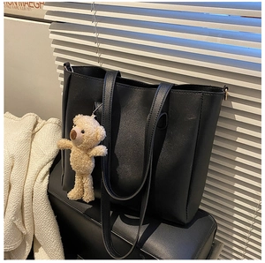 Detail of soft black leather tote bag featuring a cute beige plush bear pendant