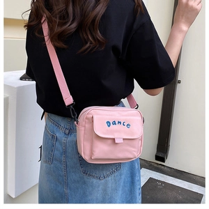 Detailed back view of pink nylon crossbody bag with blue DANCE embroidery on a model