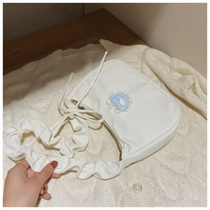 Detail of off-white fabric crossbody bag with pleated strap and blue heart patch