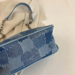 Light blue denim underarm bag with star prints and silver chain strap on cream fabric