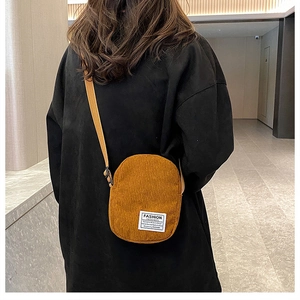 Detailed view of ginger corduroy crossbody bag with fashion label on black hoodie model
