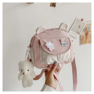 Detail of pink canvas crossbody bag with cartoon bear badges and plush bear pendant