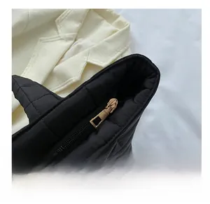 Close-up of smooth gold zipper closure on black quilted tote bag with square texture