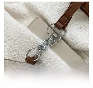 Détail de la bandoulière en cuir marron avec chaîne argentée sur un sac cabas en daim beige
