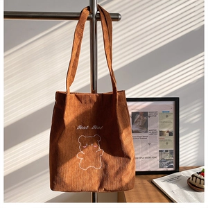 Dettaglio di borsa tote in velluto a coste marrone con ricamo di orso e luci soffuse