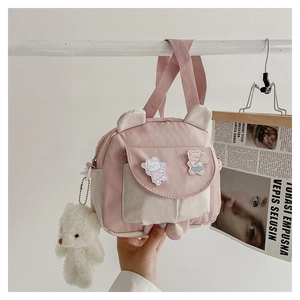 Detailed view of canvas crossbody bag with bunny ears, bear charm, and pink strap