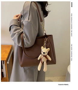 Detail of a brown leather tote bag with FASHION embossing and a cute knitted bear charm