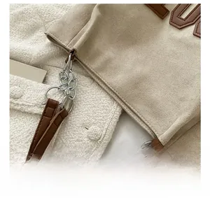 Détail de couture précise sur cabas en daim beige avec bordure en cuir marron et chaîne