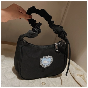 Detailansicht des gefalteten Griffs und Herz-Wal-Aufnähers an einer schwarzen Handtasche