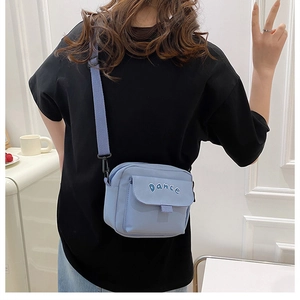 Detail of blue nylon crossbody bag featuring white Dance embroidery and adjustable strap