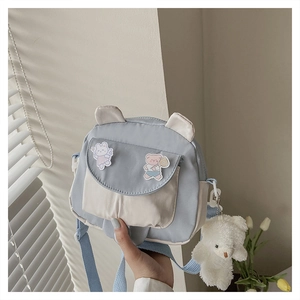 Close-up of blue and beige canvas crossbody bag with cute cartoon patches and bear charm