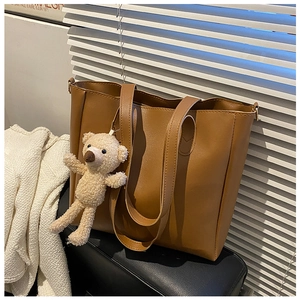 Brown leather tote bag detail with cute plush bear charm in natural window light