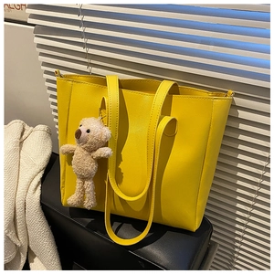 Detail of yellow soft leather tote bag with a cute plush bear charm on a black seat