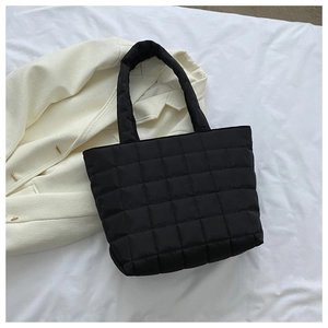 Top view of a black quilted tote bag with padded texture on a white fabric background