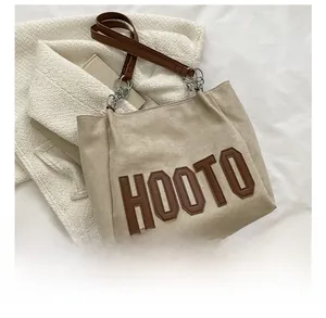 Détail du sac cabas beige montrant les anses en cuir marron et le lettrage HOOTO brodé