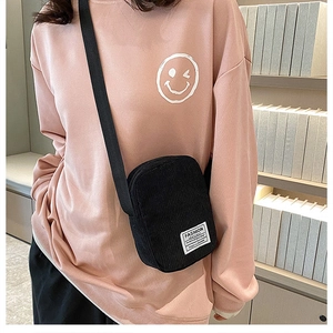 Detail of black corduroy mini crossbody bag with fashion label on a pink sweatshirt