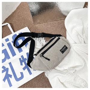 Detail of light gray corduroy chest bag with adjustable strap and fashion label tag