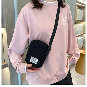 Detail of black corduroy crossbody bag featuring a fashion logo tag and adjustable strap