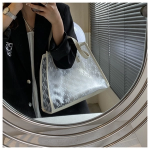 Detail of white PVC tote bag with grey M monogram pattern and leather top handles