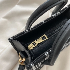 Detail einer stilvollen schwarz-weißen Tweed-Handtasche mit goldenem Reißverschluss