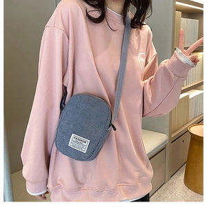 Detail of smog blue corduroy mini crossbody bag with fashion label on pink sweatshirt