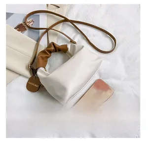 Vista dettagliata di una borsa a nuvola bianca con manici marroni accanto a uno smartphone