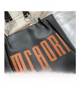 Détail du cabas noir avec broderie MCAORI orange et bandoulière en chaîne argent