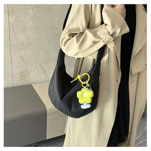 Détail d'un sac à bandoulière noir en demi-lune avec un charme de fleur jaune sur modèle