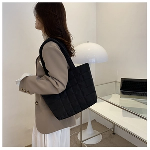 Side view of a large black quilted nylon tote bag worn by a model in a modern office set