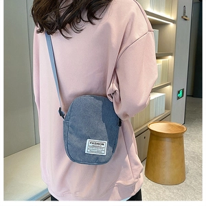 Detailed view of dark grey corduroy mini crossbody bag worn by model in casual setting