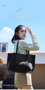 Outdoor shot of a large black faux leather tote bag against a bright blue sky background