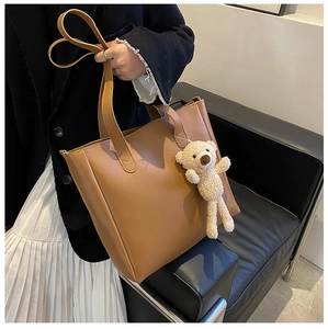 Detail shot of a caramel brown matte leather tote bag featuring a cute cream teddy bear charm