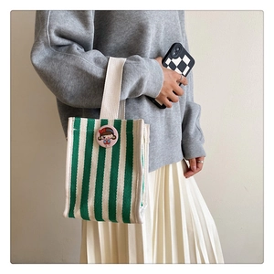 Close-up of green and white striped canvas tote bag with a pink cartoon girl badge