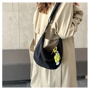 Sac croissant noir chic avec breloque fleur jaune porté sur un trench-coat beige