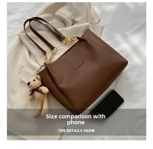 Brown tote bag size comparison with a smartphone featuring a teddy bear charm