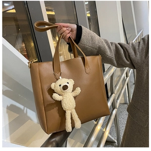 Close-up of brown soft leather tote bag with long handles and a cute plush bear charm