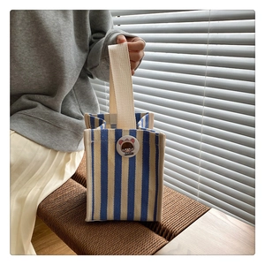 Close-up of a blue and white striped canvas tote bag with a cute badge and handle