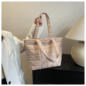 Detail of light pink quilted tote bag with dual handles on a minimalist dark surface