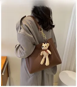 Detail of dark brown PU tote bag with gold chain strap and beige bear charm on model